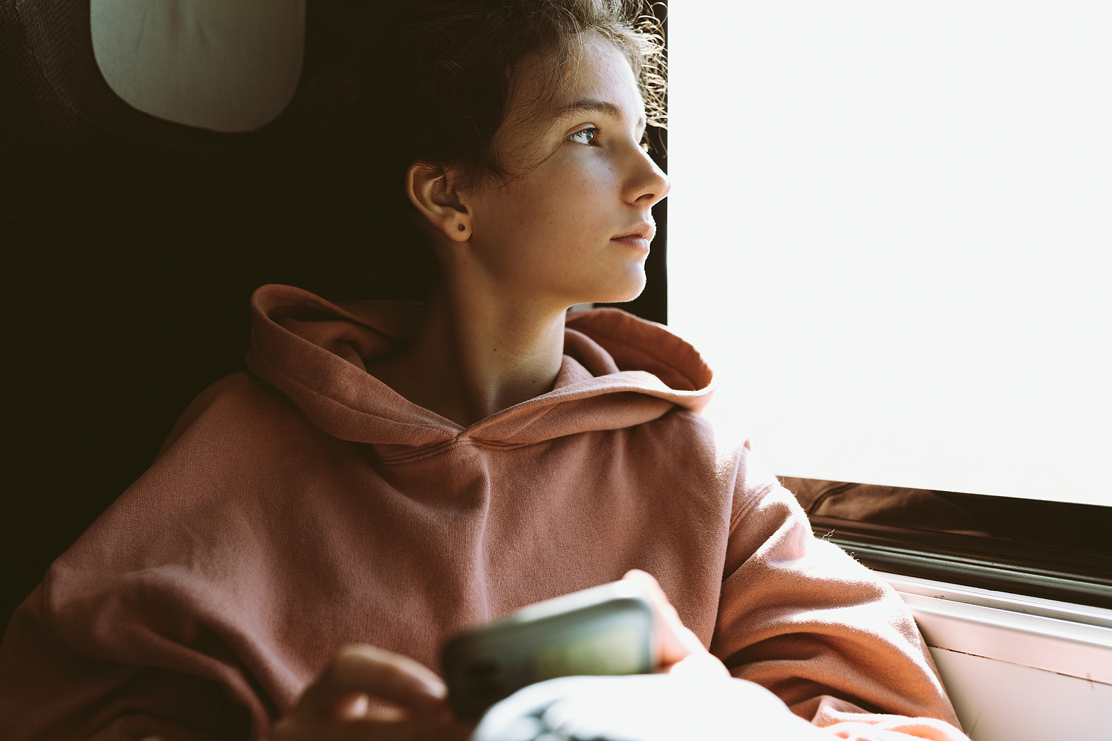 Teenage Girl In Warm Pink Sweatshirt Sits Near Window In Train