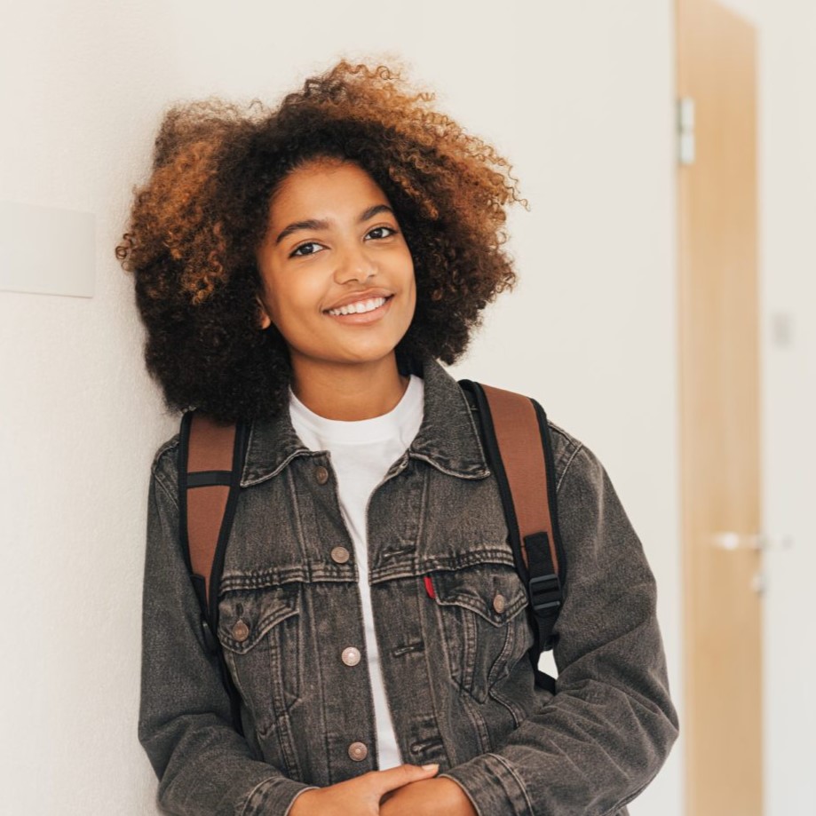 Young black student leaning against wall and smiling
